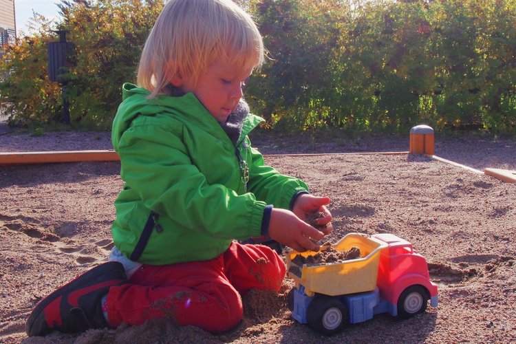 Lapsi leikkii hiekkalaatikolla leluautolla.