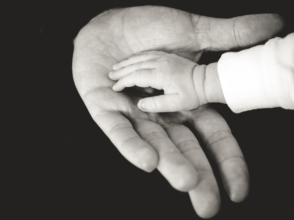 Mustavalkoinen kuva, lapsen käsi isän kädessä.