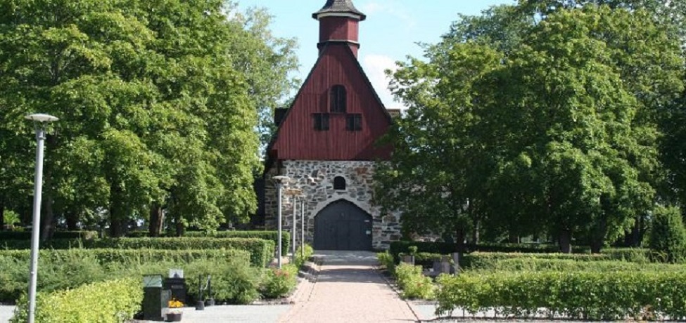 Kirkon edestä otettu kesäinen kuva. Kuvassa näkyy kirkon pääovi.