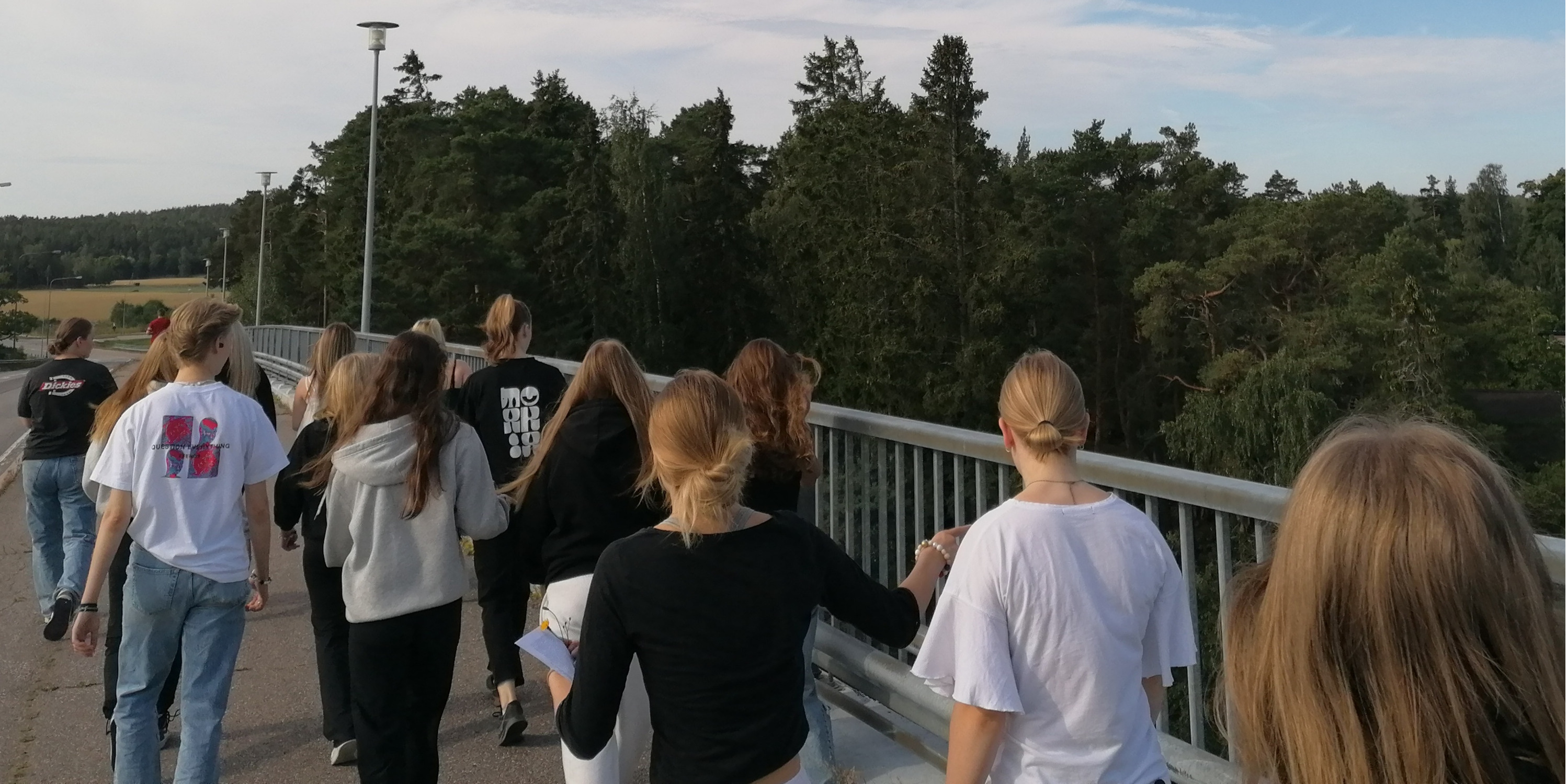 Ryhmä nuoria kuvattuna takaapäin kävelemässä sillalla kesäisenä päivänä.