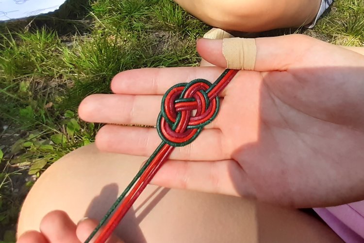 Nahkanauhoista solmittu leirikoru lapsen kämmenellä.