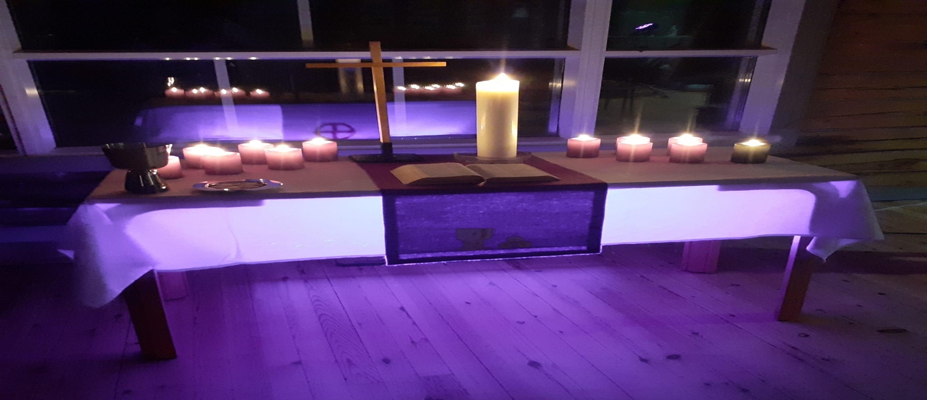 Viherlahden leirikirkon alttarilla Raamattu, risti, kynttilöitä ja ehtoollisvälineet. Valaistus violetti.